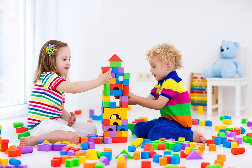 Two children playing with colorful building blocks on a white floor.