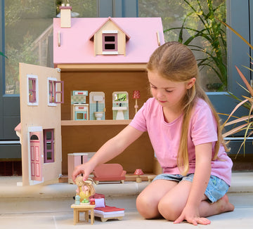 A young girl playing with a wooden dolls house, sparking imagination.